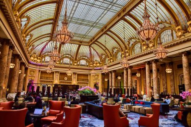 Altın turuncu avizeler ve tavana doğru sütunlarla süslü salonda oturan insanları hayal edin.