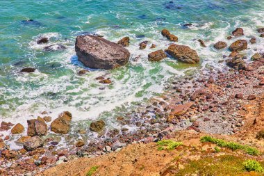 Dalgalar ve deniz köpüğü ile çimenli tepenin yakınındaki kayaların etrafında dönen Rocky Shore görüntüsü