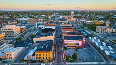 S Walnut Street Muncie 'nin görüntüsü, şehir merkezindeki binalarda günbatımında kilise ve su kulesiyle birlikte.