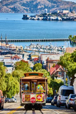 Trolley 'nin dik, güneşli yolda San Francisco Körfezi' nde Alcatraz Adası 'yla birlikte gittiği görüntüsü.