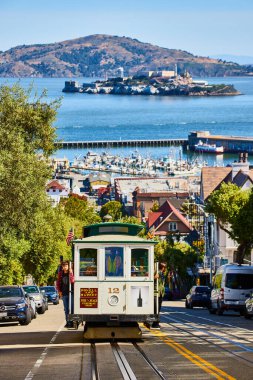 Trolley 12 'nin görüntüsü uzak rıhtımla yokuş yukarı gidiyor ve arkasında Alcatraz Adası var, San Francisco, CA