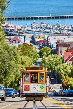 Güneşli bir günde San Francisco Körfezi ve limanı ile birlikte tramvayda tepeye çıkan turistlerin görüntüsü