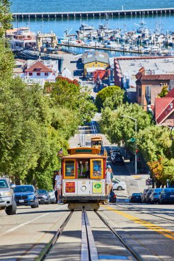 İnsanlar güneşli bir günde limandan yokuş yukarı giderken ellerinde tırabzan tutan turistlerin olduğu Trolley 'nin görüntüsü