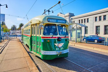 Öndeki yeşil Castro tramvayı, 29 nolu rıhtımın yanında üzerinde elektrik kabloları olan San Francisco Caddesi, CA
