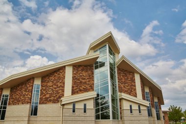 Sıcak tonlu tuğla kaplamalı modern kilise binası, cam bir atriyum ve dinamik bir gökyüzü arkaplanı - emlak, eğitim ve kurumsal materyallerde ulaşılabilirlik ve modernliği sergilemek için mükemmel.