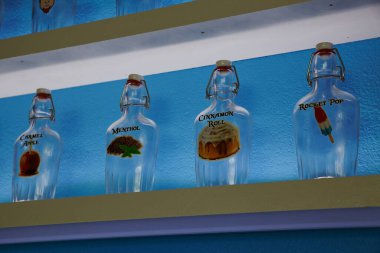 Sergilenen canlı tatlar: Modern, desenli mavi bir duvara karşı Carmel Apple, Menthol, Cinnamon Roll ve Rocket Pop etiketli dört cam şişe koleksiyonu