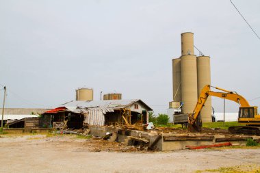 Değişim ve çürümenin sembolü, sarı bir CAT kazıcısı Evansville, Indiana 'da terk edilmiş bir binayı yıkıyor. Harabelerin arasında, yükselen silolar endüstriyel geçmişteki bölgeleri hatırlatmak için duruyor..