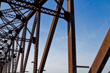 Louisville, Kentucky 'deki heybetli çelik köprünün yakın çekim görüntüsü. Metal kirişlerin ve perçinlerin açık mavi gökyüzüne karşı karmaşık desenleri köprülerin ihtişamını gözler önüne seriyor.