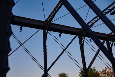 Çarpıcı çelik köprü, birbirine kenetlenmiş karmaşık kirişler ve mavi ışıklar, Fort Wayne, Indiana şehir merkezinde huzurlu bir mavi saate karşı sallanıyor. Mühendislik icatları için mükemmel.