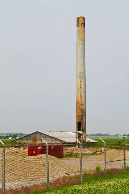 Evansville, Indiana 'da terk edilmiş bir sanayi bölgesinin solmuş ihtişamını yakalamak. İhmal edilmiş bir deponun üzerine yükselen bir baca yığını, sakin kırsal alanda endüstriyel temaları çağrıştırıyor.