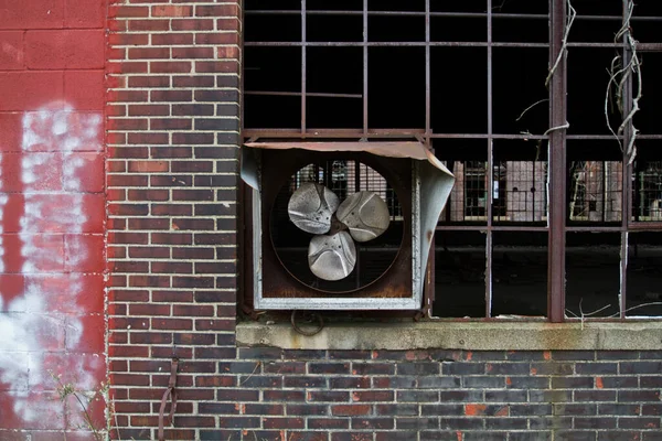 Rusted industrial fan in abandoned brick building, Warsaw. A haunting scene of urban decay and nature reclaiming, capturing the passage of time and resilience amidst neglect.