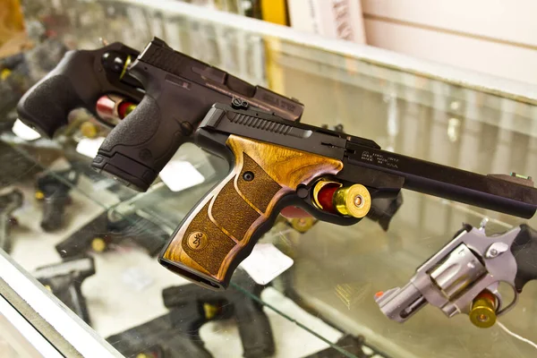 Exquisite craftsmanship meets modern design. A wood-grain grip handgun with loaded cylinder steals the spotlight among a variety of firearms in a well-lit gun shop in Hudson, Indiana.