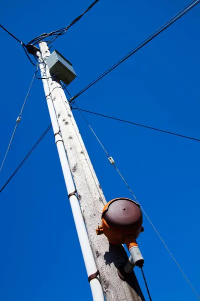 Essential urban infrastructure: A weathered utility pole stands tall against a vibrant blue sky in Empire, Michigan. Highlighting the intricate network of power lines and electrical equipment, this