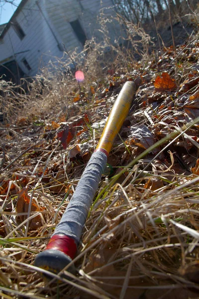 秋叶覆盖地面上的老式棒球拍在废弃房屋背景下的应用 — 图库照片
