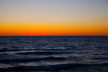 Dusk 'ta sakin bir Michigan Deniz Burnu: Güneş ufuktan batarken engin okyanusa bakan sakin bir alacakaranlık saati, gradyan gökyüzünde ılık turuncu bir parıltı yayıyor..