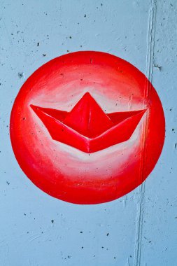 Canlı sokak sanatı, şehir yaratıcılığının ruhunu, desenli beton bir duvarı süsleyen kırmızı kağıt bir tekneyle yakalıyor. Bilinmeyen bir şehirde oyuncu ve yaratıcı bir sahne..