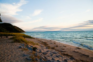 Huzurlu sahil cenneti: Sakin bir gün doğumu ya da gün batımı, yemyeşil bir yamaçla çerçevelenmiş ve ıssız bir ahşap bankla tamamlanmış el değmemiş kumlu bir plajı aydınlatır..