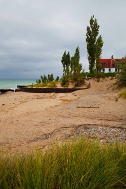 İnzivaya çekilmiş deniz kenarı inzivası, büyüleyici kırmızı çatılı bir ev, rüzgarla süpürülmüş ağaçlar ve dingin bir göl manzarası Michigan kırsalında huzur ve doğal güzellik sunuyor..