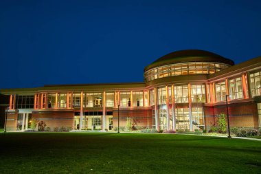 Alacakaranlıktaki modern eğitim binası, çarpıcı mimari ve sıcak yapay ışıklandırma. Fort Wayne, Indiana kampüs tesisinde koyu renkli kubbeli baskın bir dairesel bölüm var.