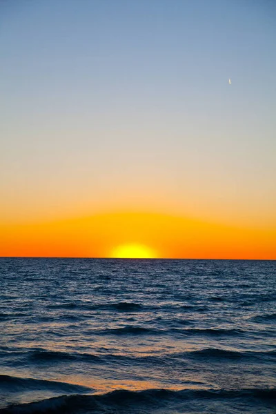 Tranquil sunset over the ocean, with vibrant hues of orange and yellow painting the sky. The calm waves reflect the golden hour glow, creating a serene atmosphere. Ideal for conveying peace, closure