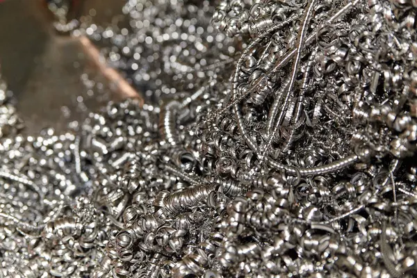 Close-up of varied metal shavings and scraps in an industrial setting, reflecting light and showcasing intricate details. Captures manufacturing waste, recycling, and material reuse.