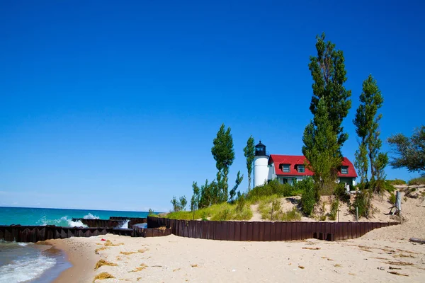 Stock image Experience the beauty of Michigans coastal landscape with this vibrant image of a charming lighthouse and keepers house perched on a sandy dune. Against a backdrop of clear blue skies and a tranquil