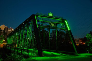 Fort Wayne, Indiana 'daki Wells Caddesi Köprüsü' nün büyüleyici gece manzarası. Canlı yeşil ışıklarla aydınlatılmış. Karmaşık metal ve mimari güzelliğini gözler önüne seriyor..
