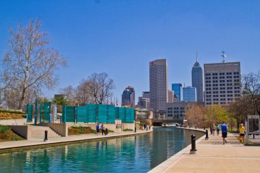 Indianapolis 'teki hareketli şehir manzarası: Huzurlu kanal, yayaların güneşli bir günde gezinti güvertesinde sakin bir şekilde gezinirken şehrin ufuk çizgisini yansıtıyor.