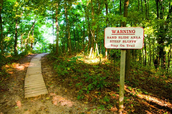Explore the untamed wilderness of Empire, Michigan Follow the well-marked trail through lush foliage and admire the warning sign highlighting the beauty and potential dangers of this sand slide area