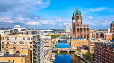 Milwaukee 'deki çeşitli mimarinin havadan görünüşü, tarihi ve modern binalardan, berrak mavi gökyüzünün altında, belirgin yeşil çatılı bir yapı, hareketli şehir manzarasına ve nehir kenarına bakıyor.