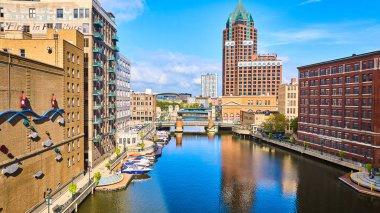 Milwaukee nehir kenarının canlı gündüz görüntüsü, tarihi ve modern mimari, yaya köprüsü ve DJI Mavic 3 insansız hava aracı ile yakalanan sakin deniz manzarası.