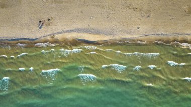 Güneşli bir günde kumsalda turistlerin kumsalda seyahat ettiği yeşil su dalgalarının üzerindeki hava görüntüsü
