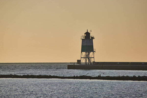 Image of Sunrise behind lighthouse at dawn with soft golden sky and Lake Michigan water in ocean endlessness