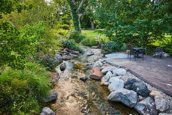 Tranquil 2023 Garden Scene in Elkhart, Indianas Botanic Gardens, Featuring a Natural Stream, Lush Greenery, and Outdoor Patio