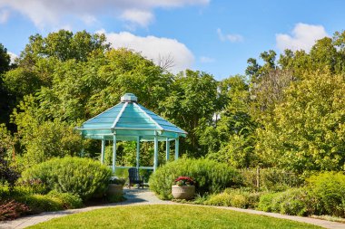 Turkuaz taraça Elkhart, İndiana Botanik Bahçeleri 'ndeki sakin parkta, yemyeşil ve çiçek açan çiçeklerle çevrili, 2023' te açık mavi bir gökyüzünün altında..