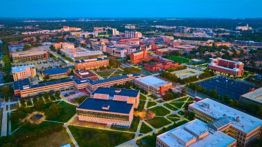 Yayılan modern Indianapolis Üniversitesi kampüsünün akşam manzarası gün batımının sıcacık parıltısıyla aydınlanıyor.