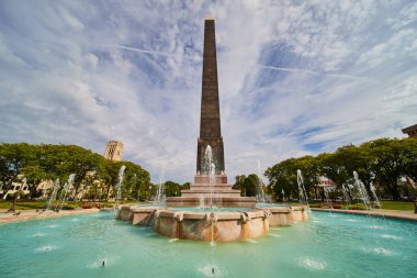 2023, Indianapolis Plaza şehir merkezindeki hareketli bir fıskiyeyle çevrili, altın uçlu büyük bir dikilitaş anıtın güneşli günü manzarası.