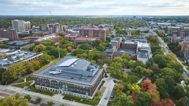 Ann Arbor 'daki Michigan Üniversitesi kampüsünün hava manzarasında modern ve geleneksel mimari, bereketli sonbahar yaprakları ve Amerikan bayrağı sergileniyor.