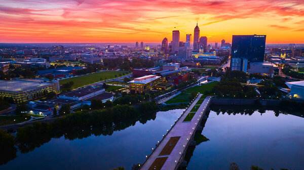 Scenic aerial view of Indianapolis skyline at golden hour, reflected in serene White River, captured by drone