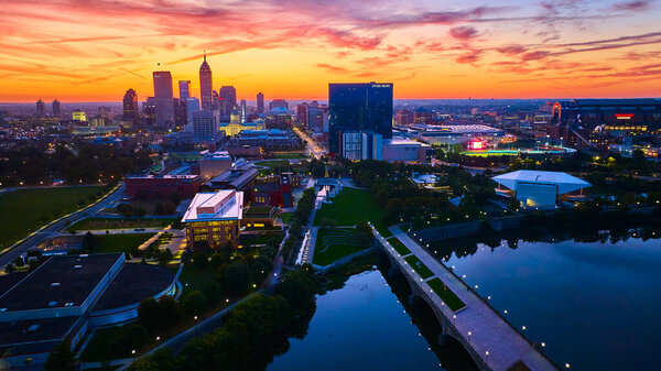 Vibrant Sunrise Over Indianapolis Skyline: Aerial View of Downtown Buildings, Bridge, and River Reflection