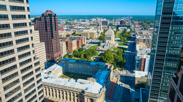 Aerial view of vibrant Indianapolis cityscape, showcasing a mix of historic and modern architecture, with focus on the Indiana War Memorial and US District Court under a clear blue sky.