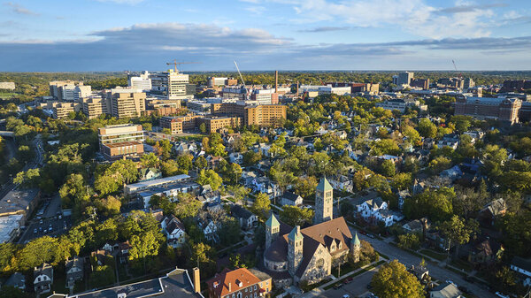 Golden hour aerial view of historic church amid residential neighborhood transitioning into bustling commercial area in Ann Arbor, Michigan