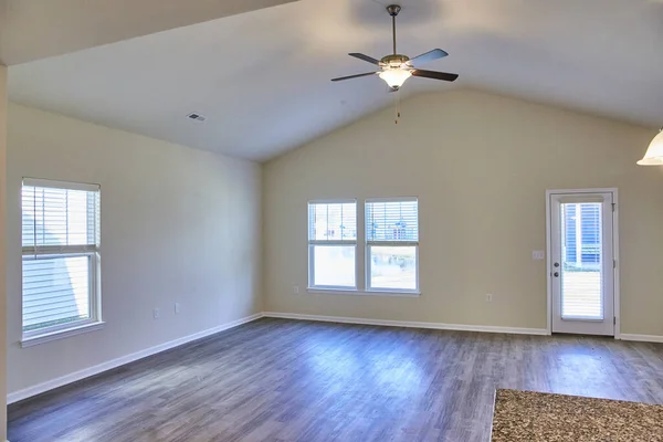 Spacious, naturally lit interior of a modern, unfurnished home in Fort Wayne, Indiana, showcasing a combination of neutral walls, grey laminate flooring, and high vaulted ceiling.