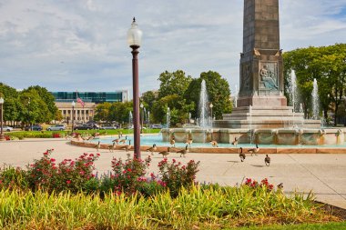 Indianapolis şehir merkezindeki güneşli sakin şehir parkında canlı çiçekler, kazlar ve 2023 'te çağdaş bir şehir zemininin yakınında süslü bir tarihi eser yer alıyor..