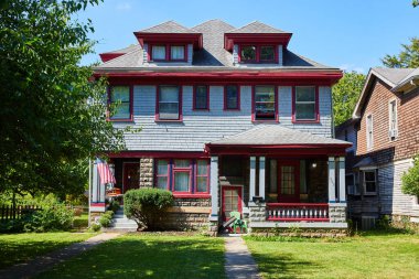 Indianapolis, Indiana 'daki klasik üç katlı Amerikan evi 2023' te yemyeşil yaz yeşiliyle çevrili, kırmızı süslemeli canlı mavi bir cephe sergiliyor.
