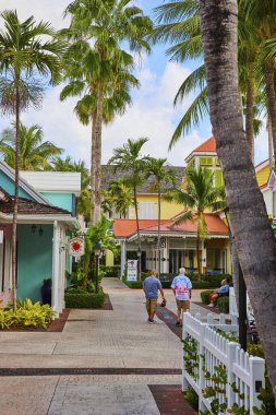 Nassau, Cennet Adası 'nda renkli binalar, yüksek palmiye ağaçları ve tatil köyünün manzarasının keyfini çıkaran sıradan yayalar olan rahat tropikal bir sokak manzarası..
