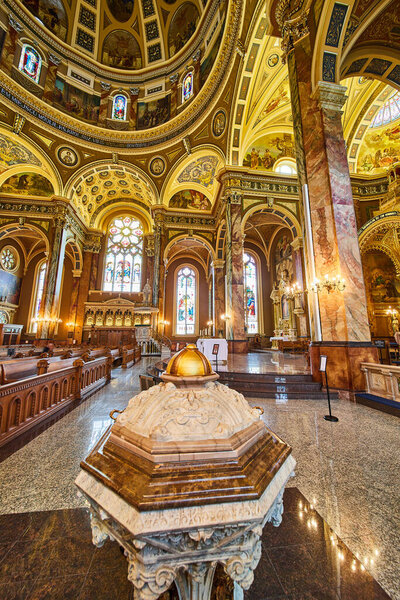 Luxurious interior of Basilica of St Josaphat in Milwaukee, featuring ornate pulpit, polished pews leading to the altar, and vibrant frescoes on vaulted ceilings.
