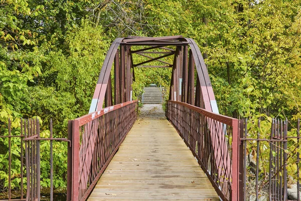 Pedestrian bridge with rustic charm in Lawton Park, Fort Wayne, Indiana, amidst lush greenery showing early signs of autumn