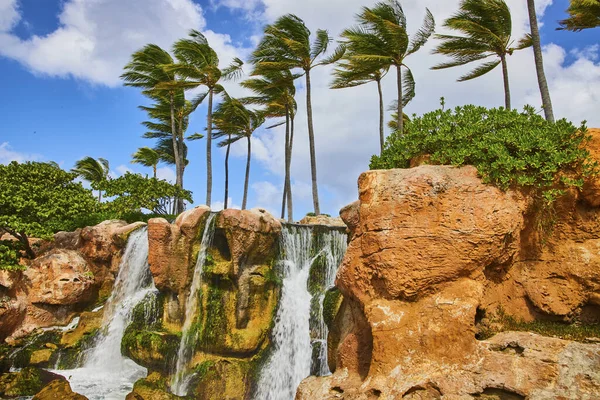 Tropical waterfall and palm trees under a sunny sky on Paradise Island, Nassau, Bahamas, symbolizing luxury resort relaxation and travel