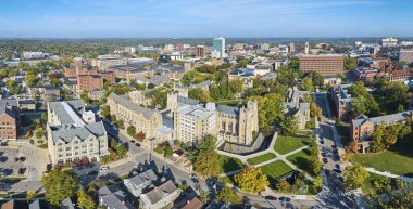 Michigan Üniversitesi kampüsünün hava manzarasında Gotik mimari, canlı sonbahar yeşillikleri ve hareketli şehir hayatı sergileniyor..